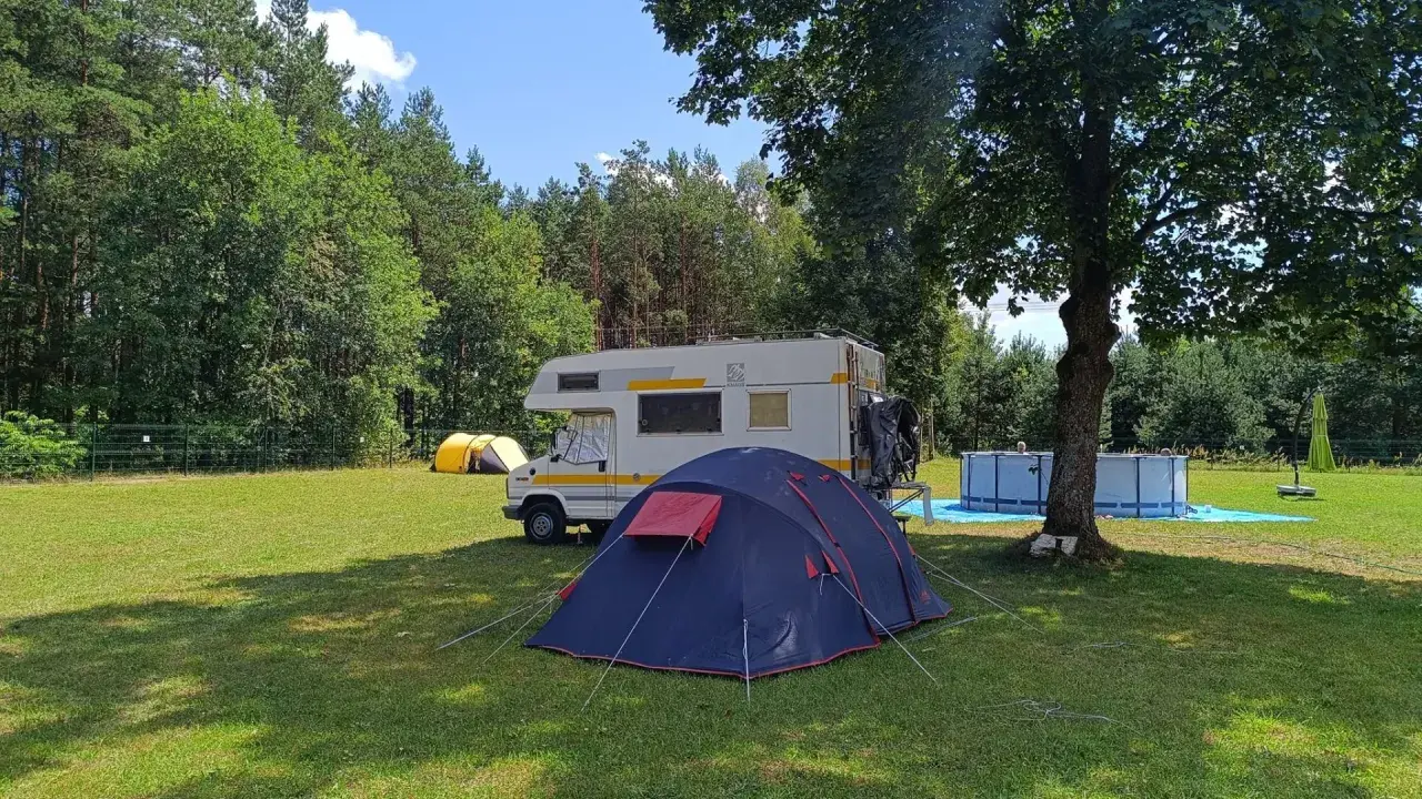 Namiot i kamper na trawie, w tle las i basen. Idealne miejsce na **camping Świętokrzyskie**.