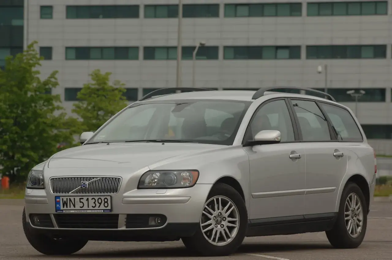Srebrne Volvo V50 kombi zaparkowane przed nowoczesnym budynkiem.