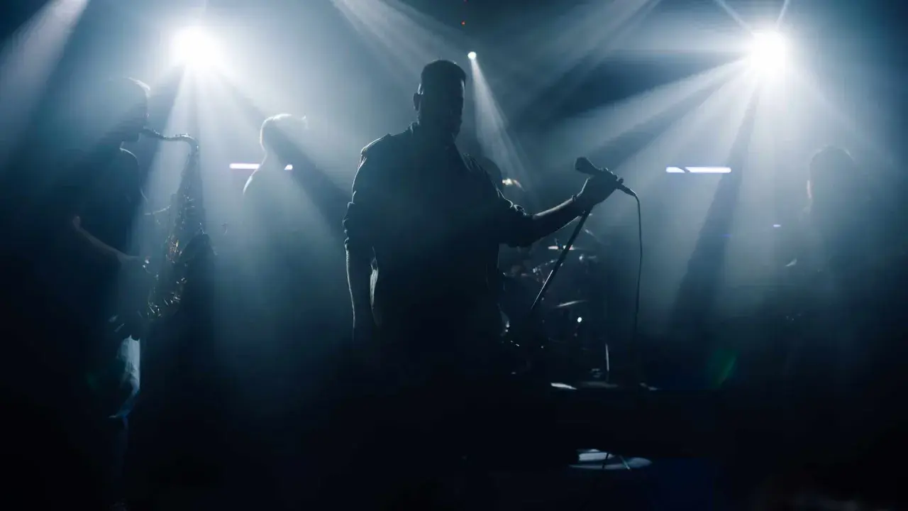 Zespół na scenie, wokalista z mikrofonem, saksofonista. Czy bilety imienne na koncert sprawdzają?