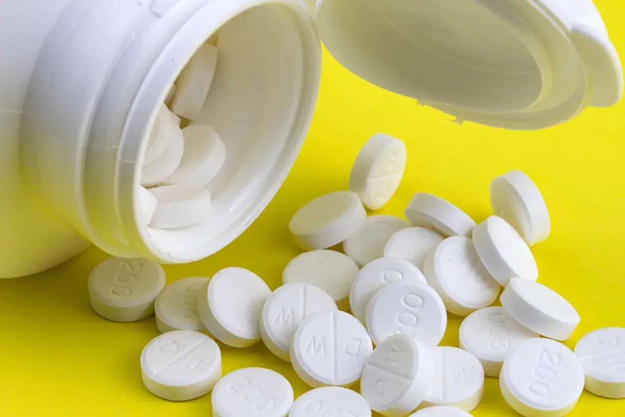 En vit burk med tabletter som kan vara adhd medicin för barn. Tabletterna ligger utspridda på en gul bakgrund.