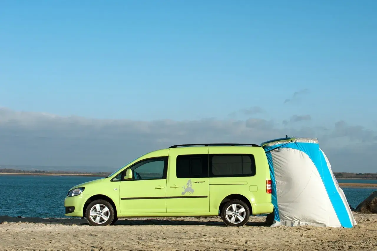 Un caddy tramper vert vif est garé sur une plage, avec une tente bleue et blanche attachée à l'arrière.