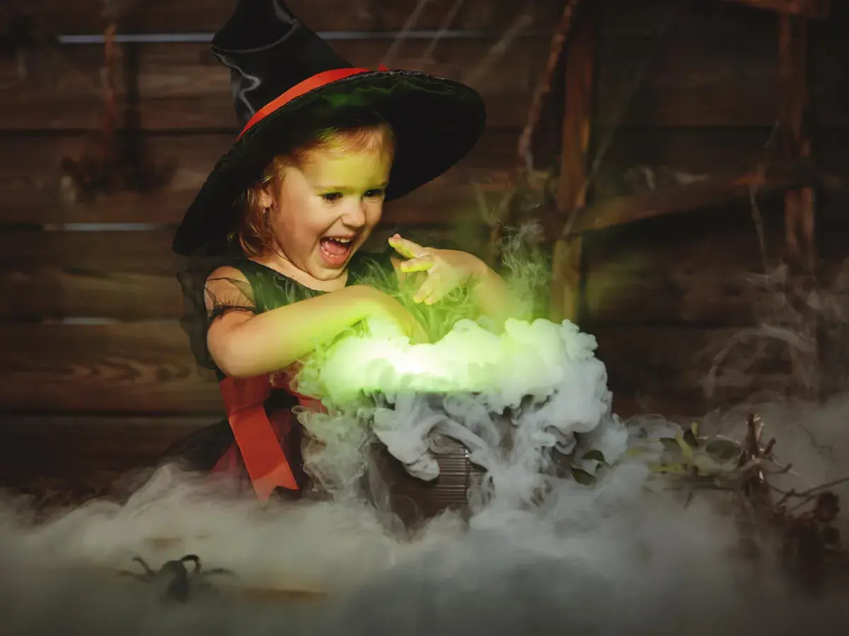 Mała czarownica w kapeluszu miesza w kociołku, tworząc zielony dym. To jak zrobic dym na Halloween!