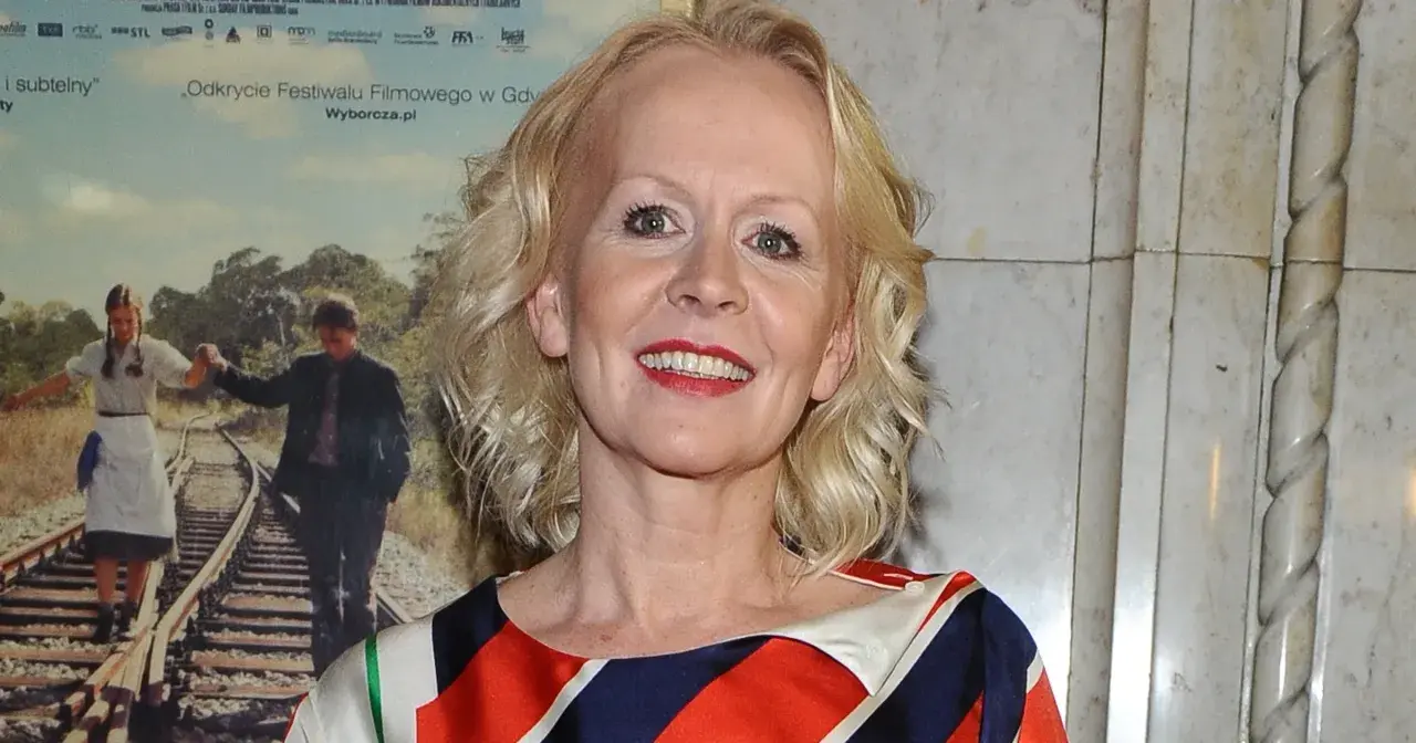 Agnieszka Krukówna uśmiecha się, ubrana w kolorowy strój. W tle plakat filmowy z parą na torach.