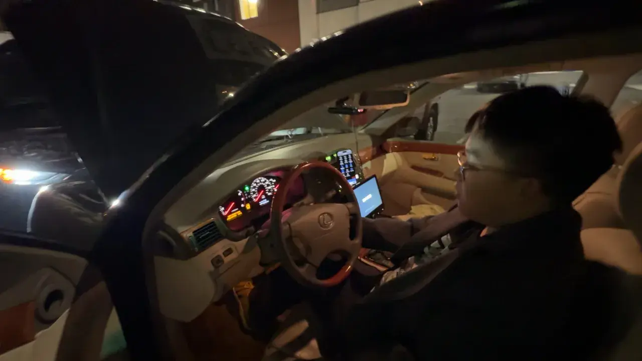 Personen försöker starta bilen som ger ett klickande ljud. Motorhuven är öppen och en laptop är ansluten till bilens system.