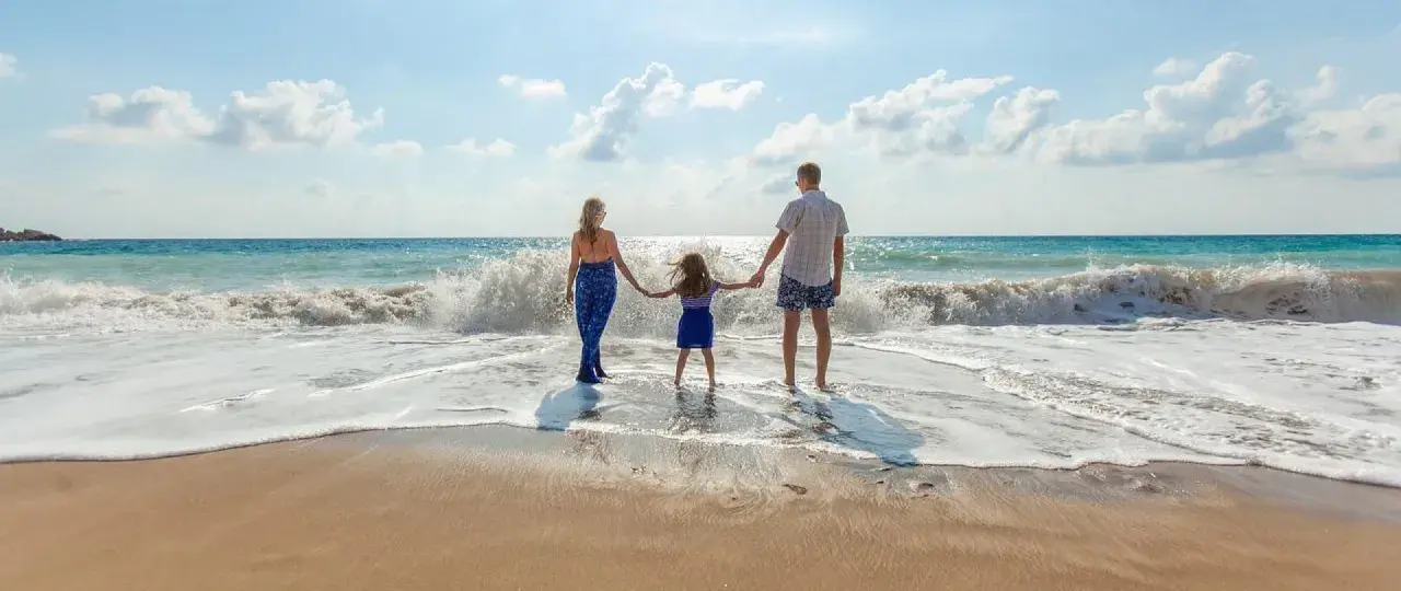 Rodzina trzymająca się za ręce na plaży, fale rozbijające się o brzeg.