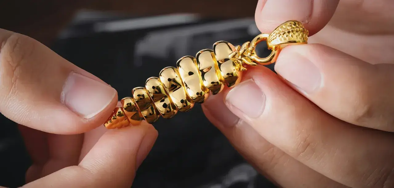 Manos sostienen un colgante dorado brillante, con forma de espiga. ¿Cómo saber si es oro? Su brillo intenso y diseño detallado sugieren autenticidad.