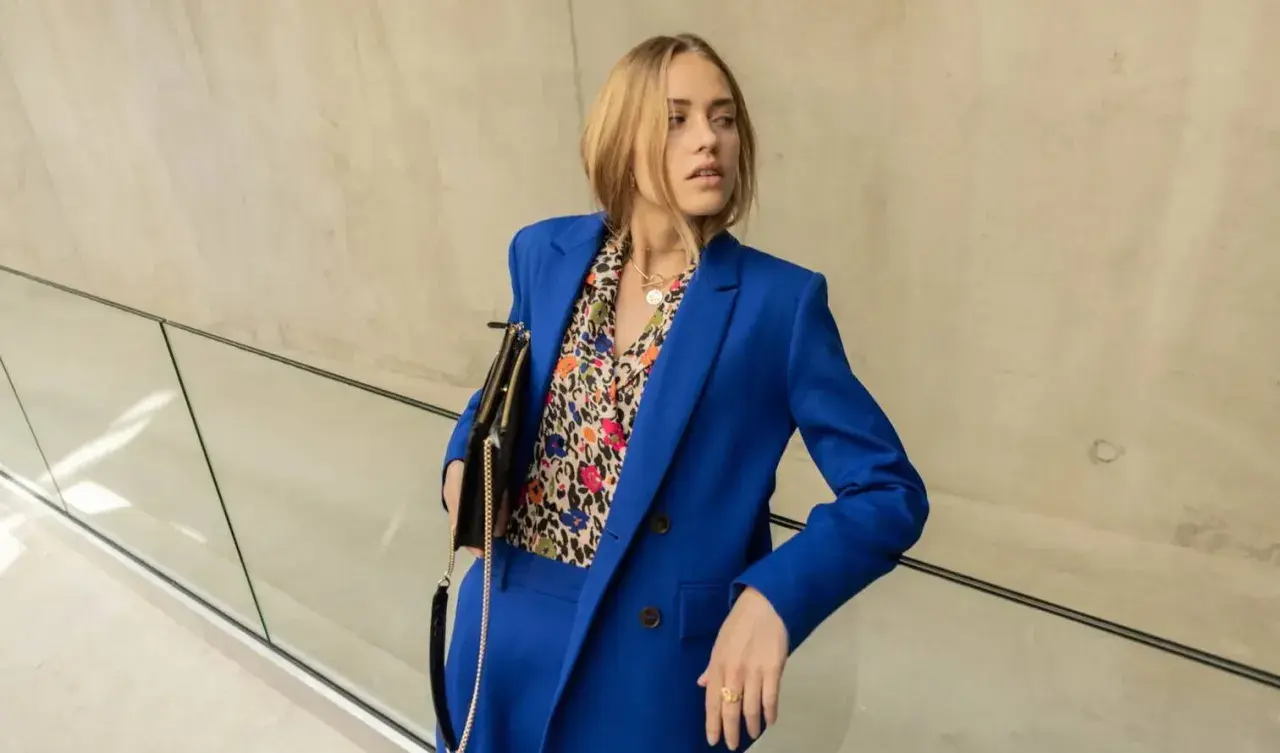 Une femme porte un tailleur-pantalon bleu vif avec une chemise à motifs colorés. Une belle idée tenue travail femme pour un look audacieux.