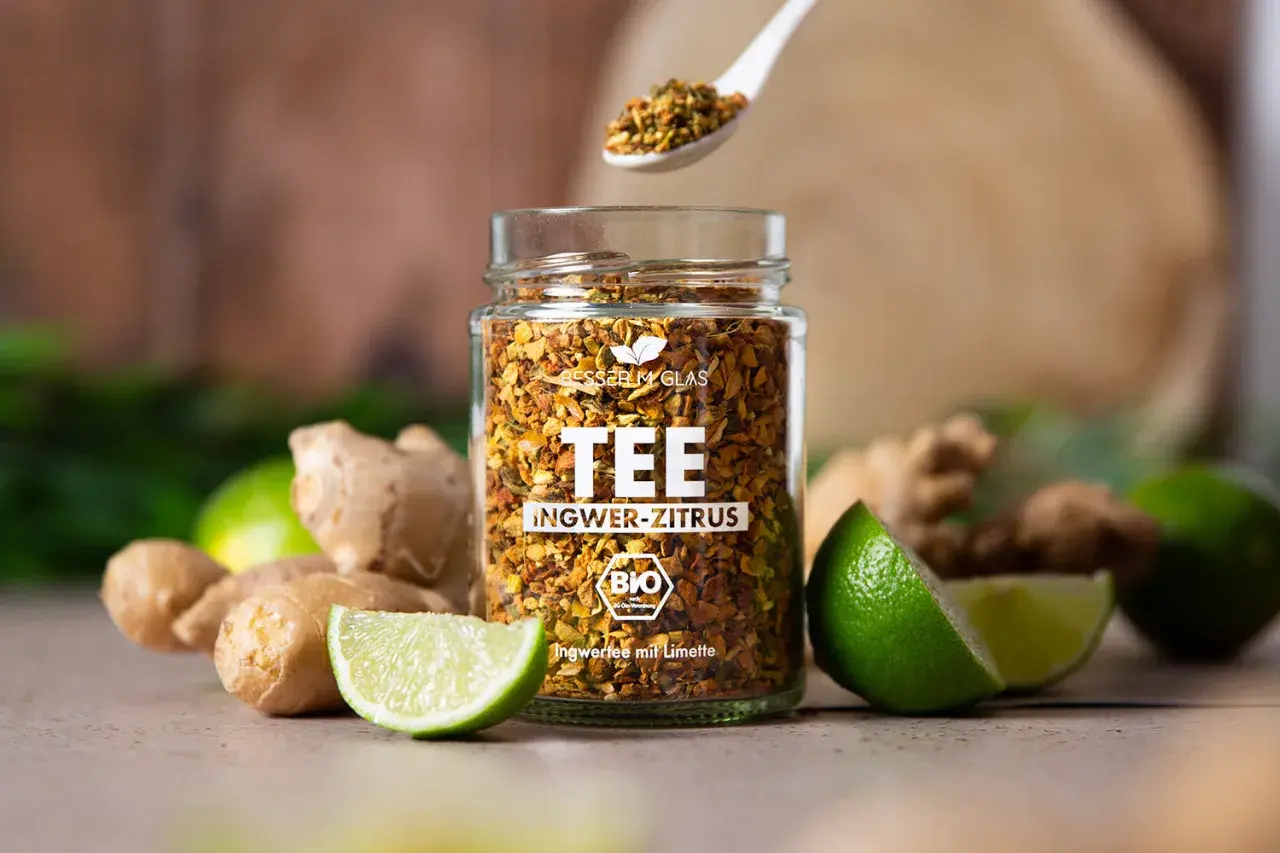 Glas mit Ingwer-Zitrus-Tee, frischem Ingwer und Limetten. Perfekt für einen wärmenden Tee, der lange ziehen kann.