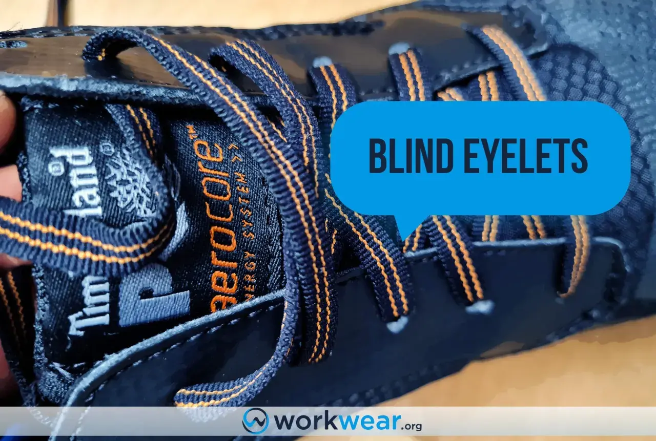 Close-up of a dark blue Timberland boot with orange stitching. The laces go through what are called blind eyelets, a feature that keeps them secure.