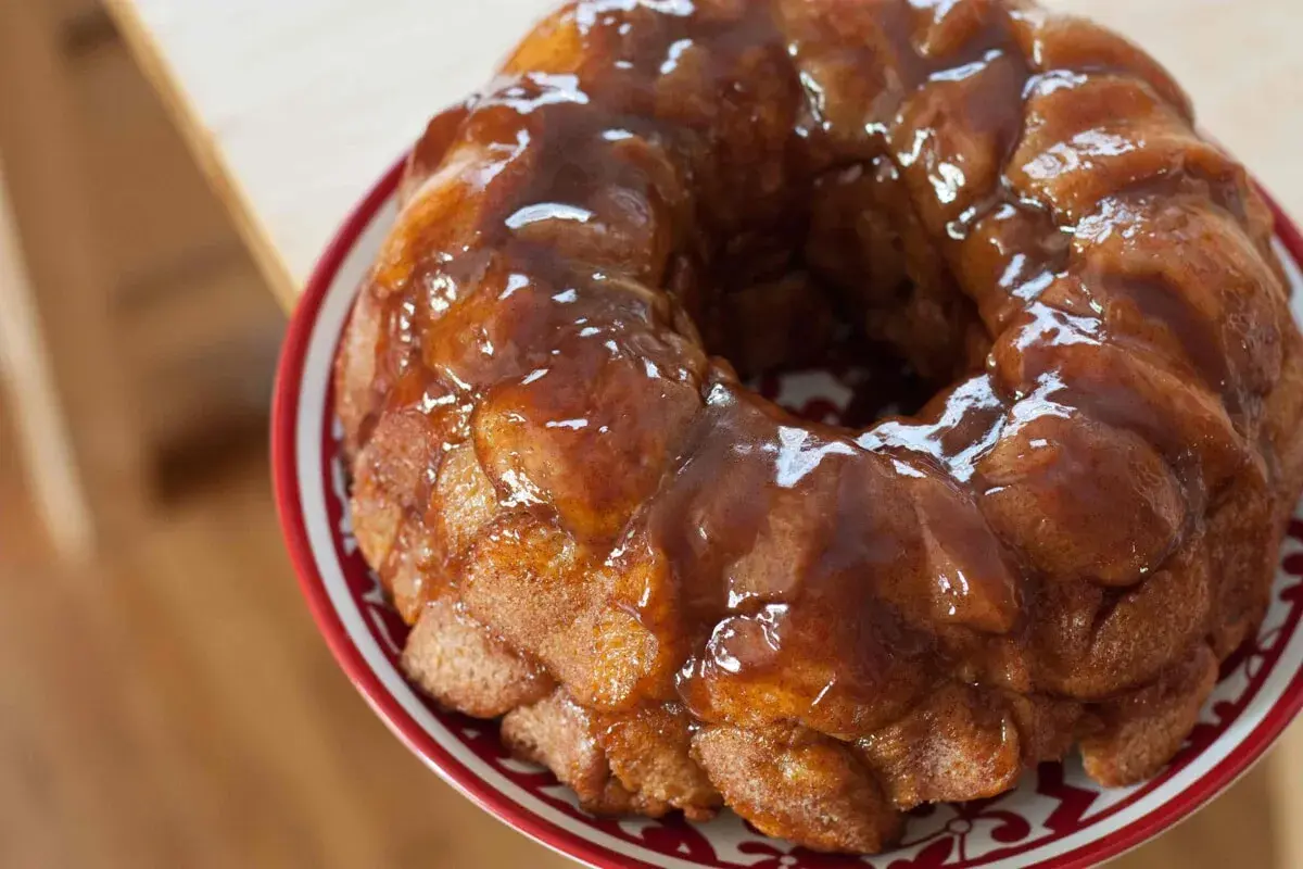 Delizioso monkey bread dorato, ricoperto di glassa lucida, servito su un piatto con bordo rosso.