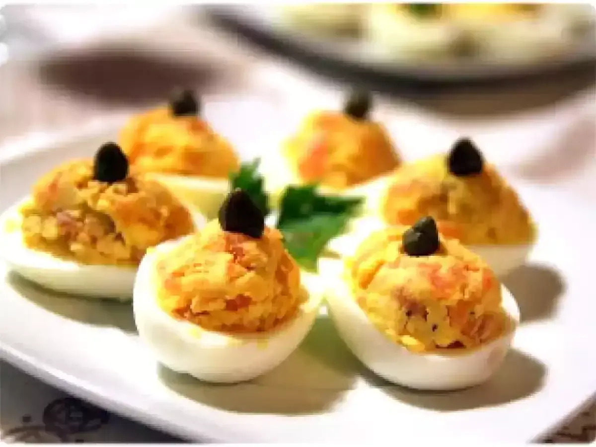 Six oeufs mimosa saumon garnis d'une olive noire sur une assiette blanche.