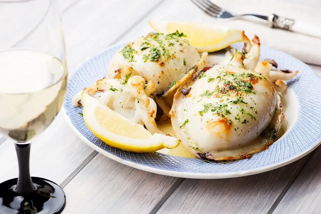 Delicioso sepia a la plancha, servido con gajos de limón y perejil picado, acompañado de una copa de vino blanco.