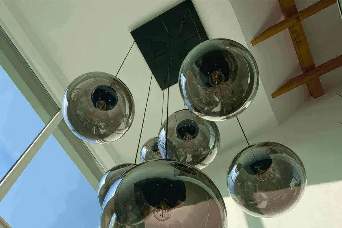 Un grupo de lámparas bola colgante de cristal ahumado cuelgan de un techo blanco, reflejando la luz y el entorno.