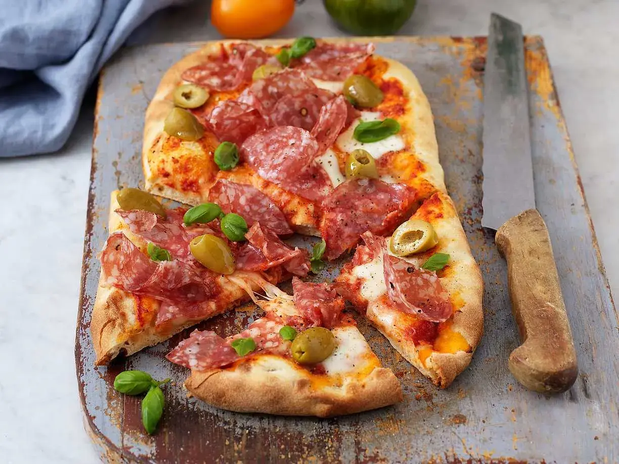 En härlig zeta pinsa med salami, oliver och färsk basilika, redo att avnjutas.