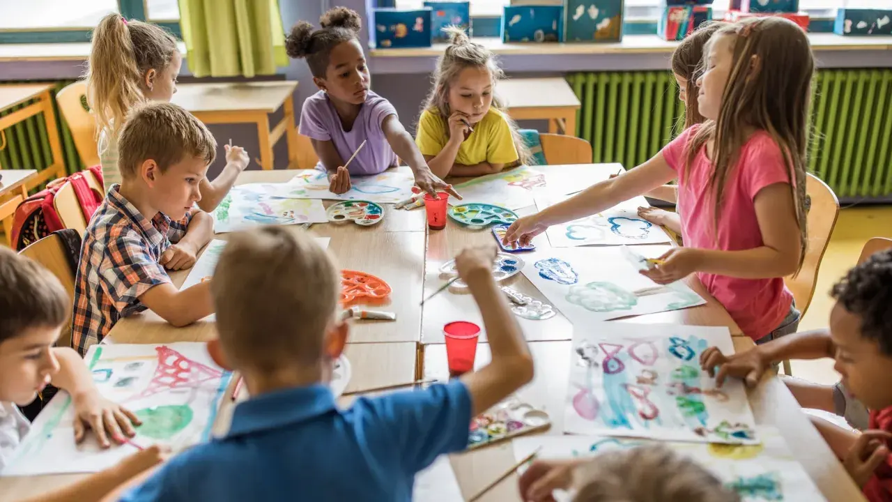 Niños y niñas disfrutan del arte en infantil, pintando con acuarelas y pinceles en una clase creativa.