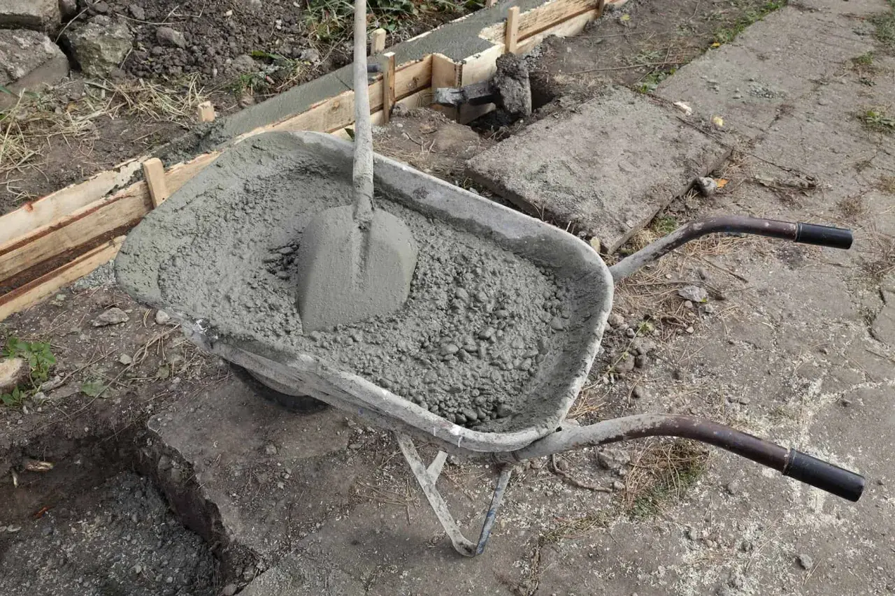 Taczka z betonem i łopatą, gotowa do wylania ławy fundamentowej. Wymiary ławy fundamentowej są kluczowe dla stabilności konstrukcji.