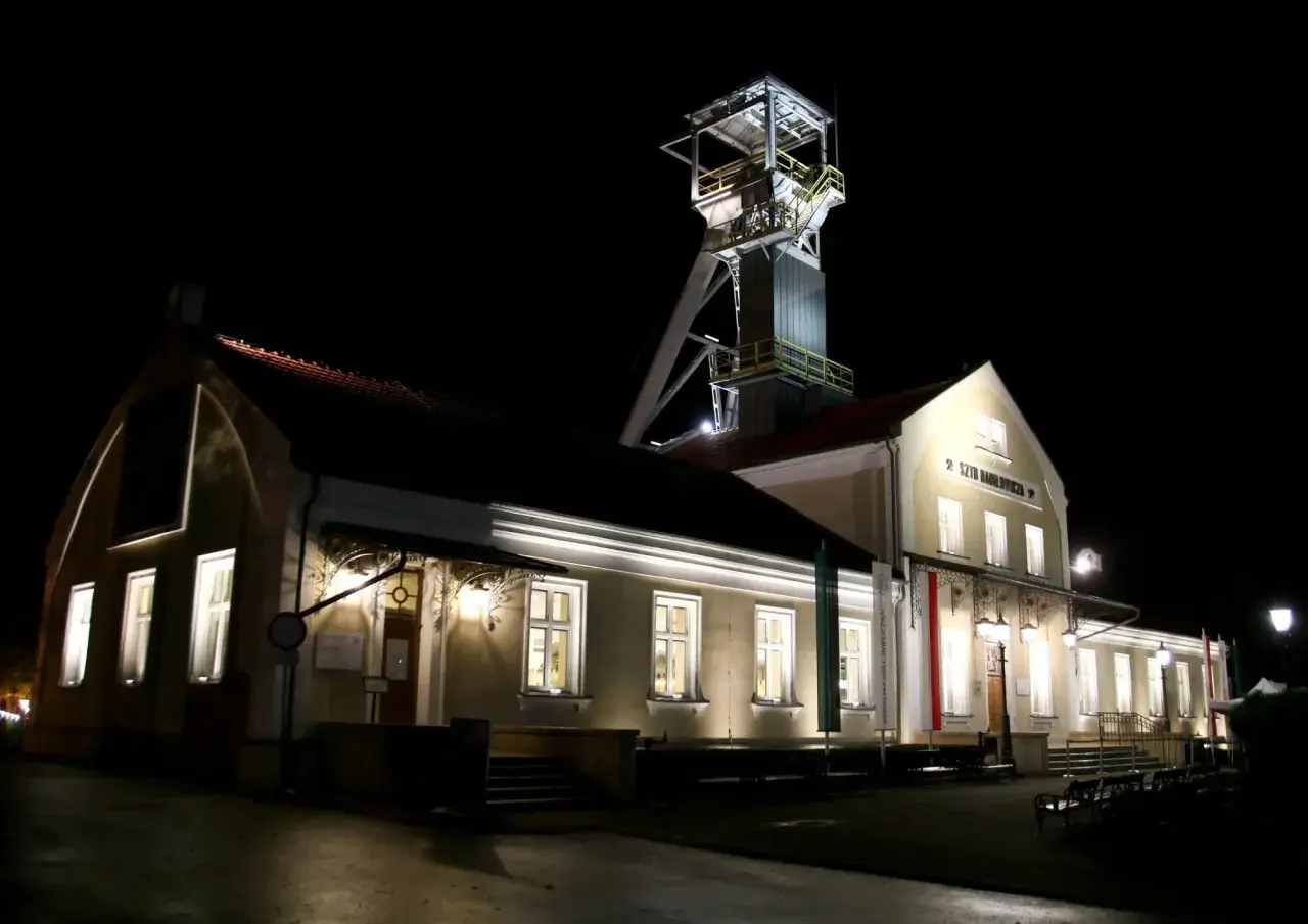 Wieczorem przy szybie kopalni Wieliczka, gdzie można kupić bilety, widać oświetlone budynki i wieżę wyciągową.