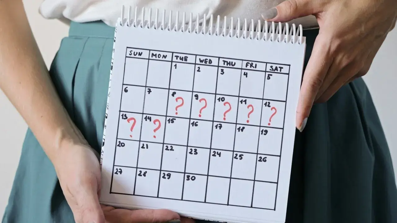 Kalender mit roten Fragezeichen, die auf unregelmäßige Zyklen und den Zusammenhang zwischen **Stress und Periode** hinweisen.