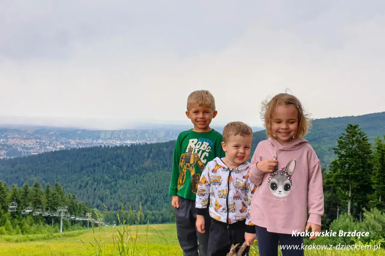 Trójka uśmiechniętych dzieci na tle górskiego krajobrazu z wyciągiem krzesełkowym. Idealne chełm atrakcje dla dzieci na wakacje.