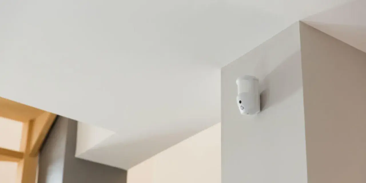 Détecteur de mouvement blanc fixé dans un coin, prêt à fabriquer une alarme.