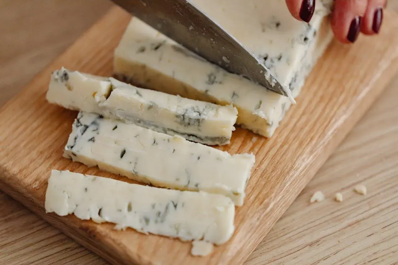 Un pezzo di gorgonzola viene affettato su un tagliere. Un desiderio di gorgonzola in gravidanza, magari per un aperitivo speciale.