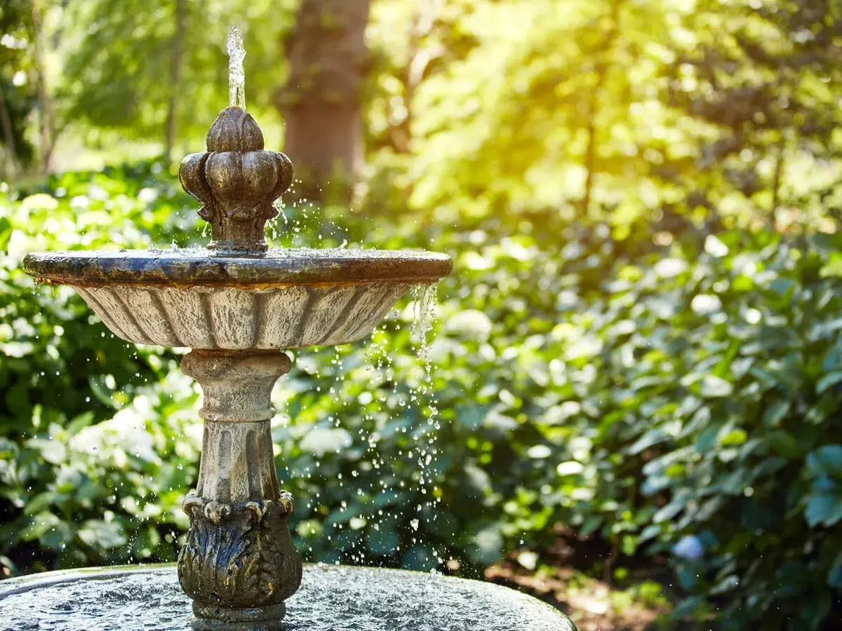 Ein antiker Gartenbrunnen sprudelt im Sonnenlicht. Tolle Ideen für Brunnen im Garten, die Ruhe und Schönheit bringen.