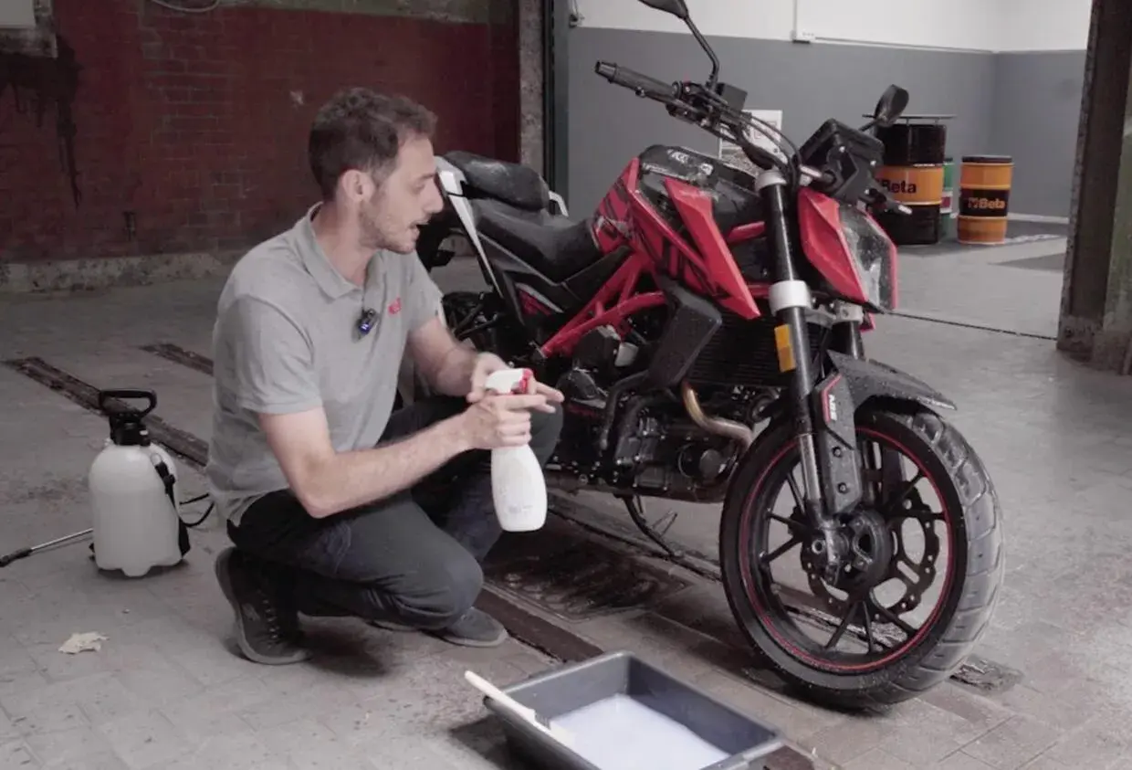 Uomo con spray e secchio di schiuma, pronto a usare prodotti casalinghi per lavare moto.