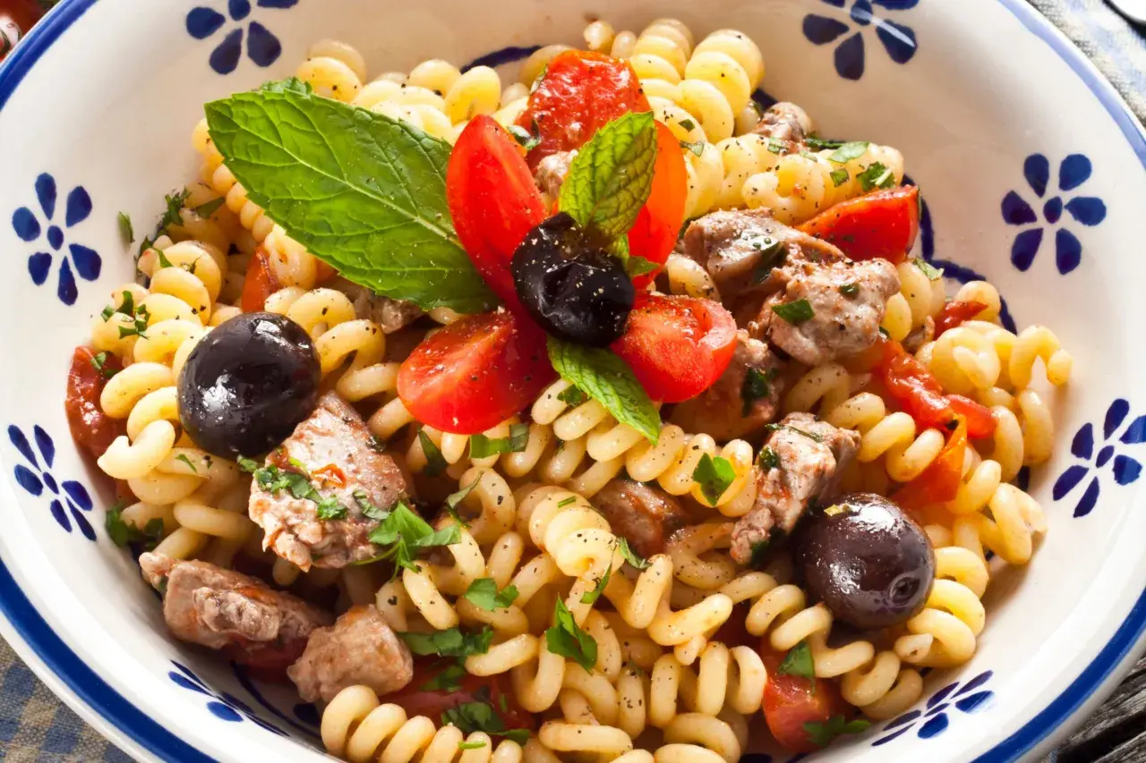 Fusilli con pesce spada, pomodorini, olive nere e menta fresca in una ciotola decorata.