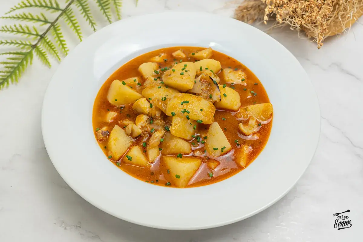 Plato de patatas con sepia, un guiso casero que evoca las patatas con sepia de la abuela, con trozos de patata y sepia en una salsa rojiza.