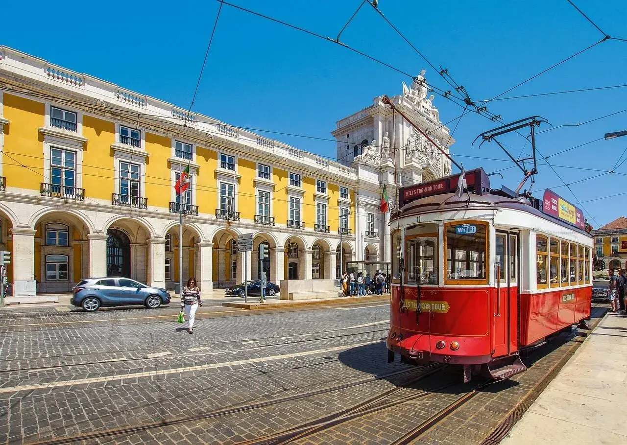 Tranvía rojo en Lisboa, listo para llevarte de Lisboa al Algarve. Edificio amarillo y arco triunfal al fondo.