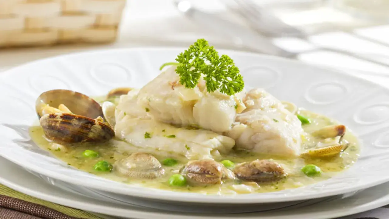 Merluza en salsa verde con almejas y guisantes, decorada con perejil fresco. Un plato marinero delicioso.