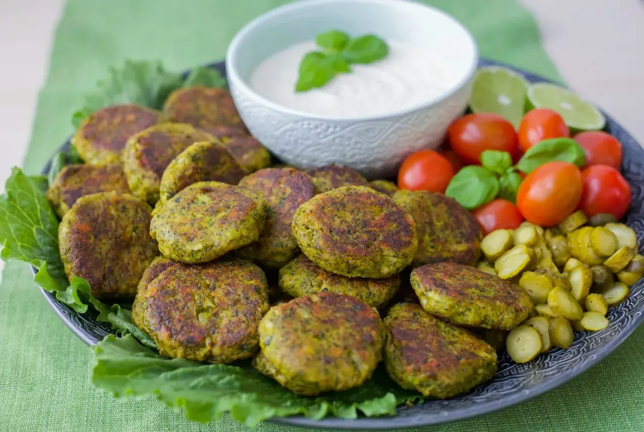 En tallrik med gyllene vegetariska biffar, serverade med en krämig dipp, körsbärstomater, gurkskivor och limeklyftor.