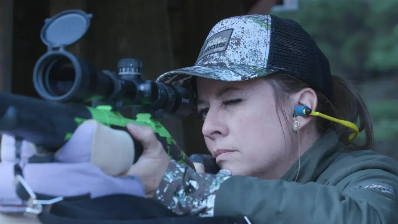 Femme concentrée visant avec un fusil de chasse, prête pour le bruit du tir.