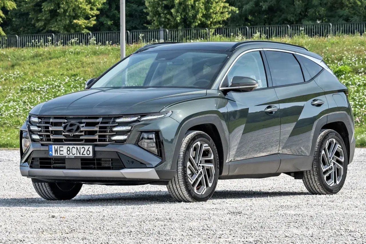 Nowy, tani SUV Hyundai Tucson w ciemnozielonym kolorze, zaparkowany na żwirowej drodze.