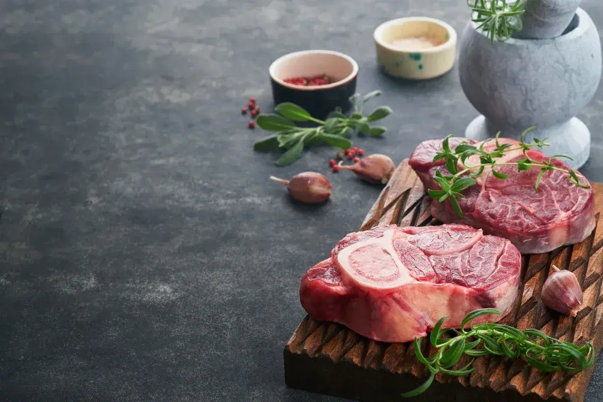 Deux grosses pièces de viande au barbecue, prêtes à être grillées, avec des herbes fraîches et de l'ail.