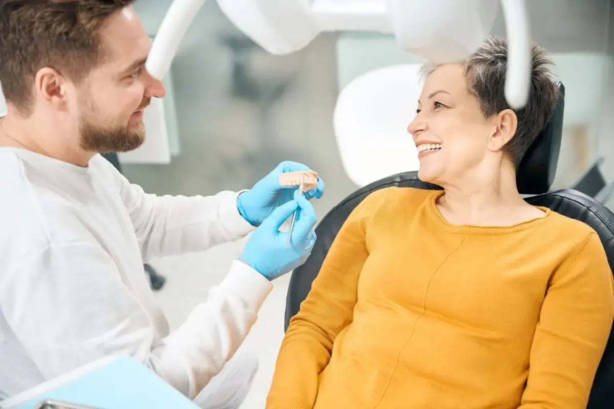 Dentista mostra un modello di denti a una paziente sorridente, discutendo di impianti dentali per un sorriso perfetto.