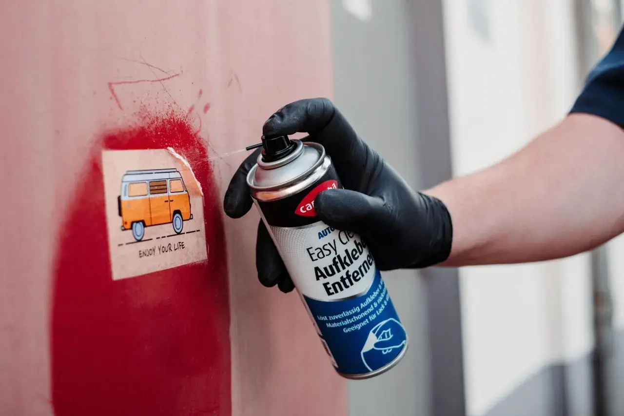 Mit einem Spray werden klebereste von kunststoffrahmen entfernt. Ein Aufkleber mit einem Camper wird gerade bearbeitet.