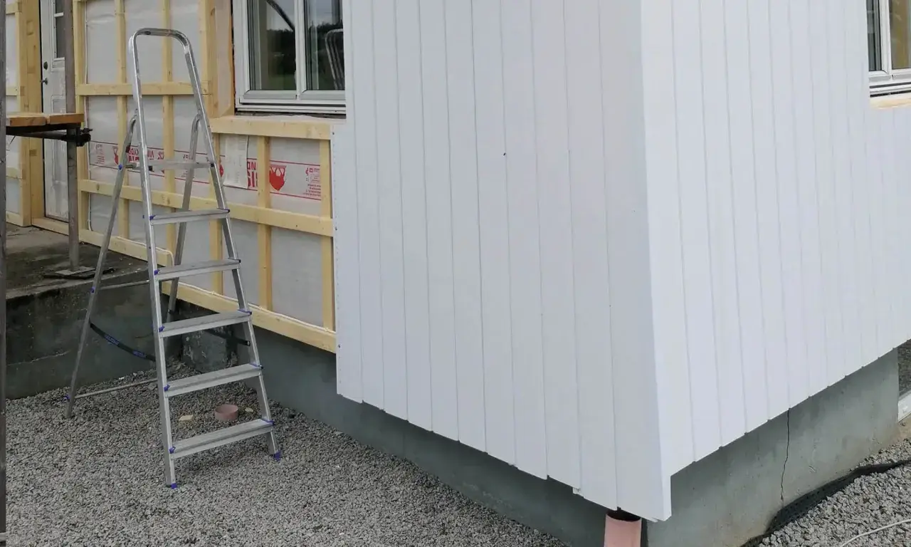 Byggarbetsplats där man valt att kombinera liggande och stående panel på husfasaden. En stege står redo.