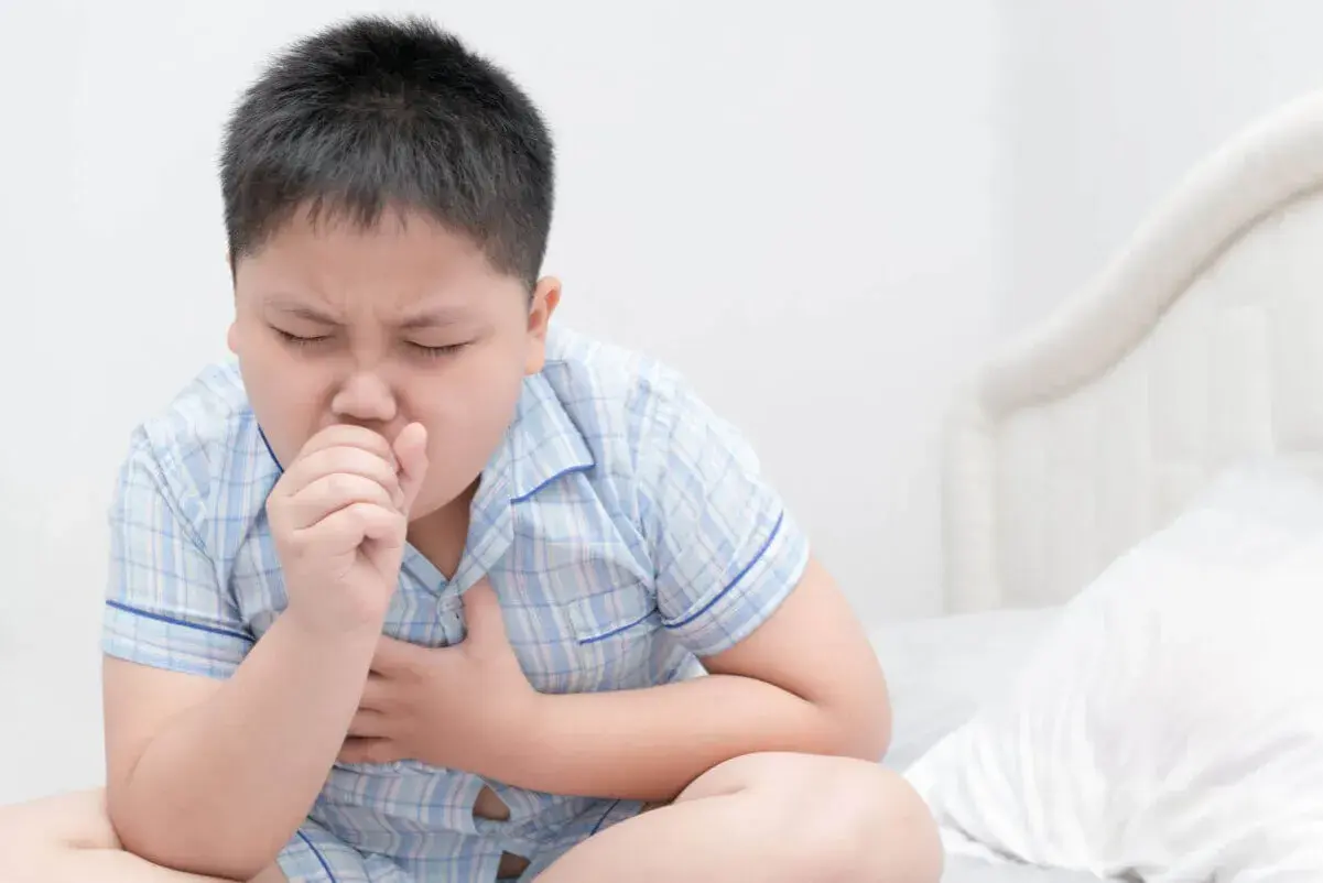 Un niño con pijama a cuadros tose con fuerza, agarrándose el pecho. Mi hijo no para de toser, parece que necesita ayuda.