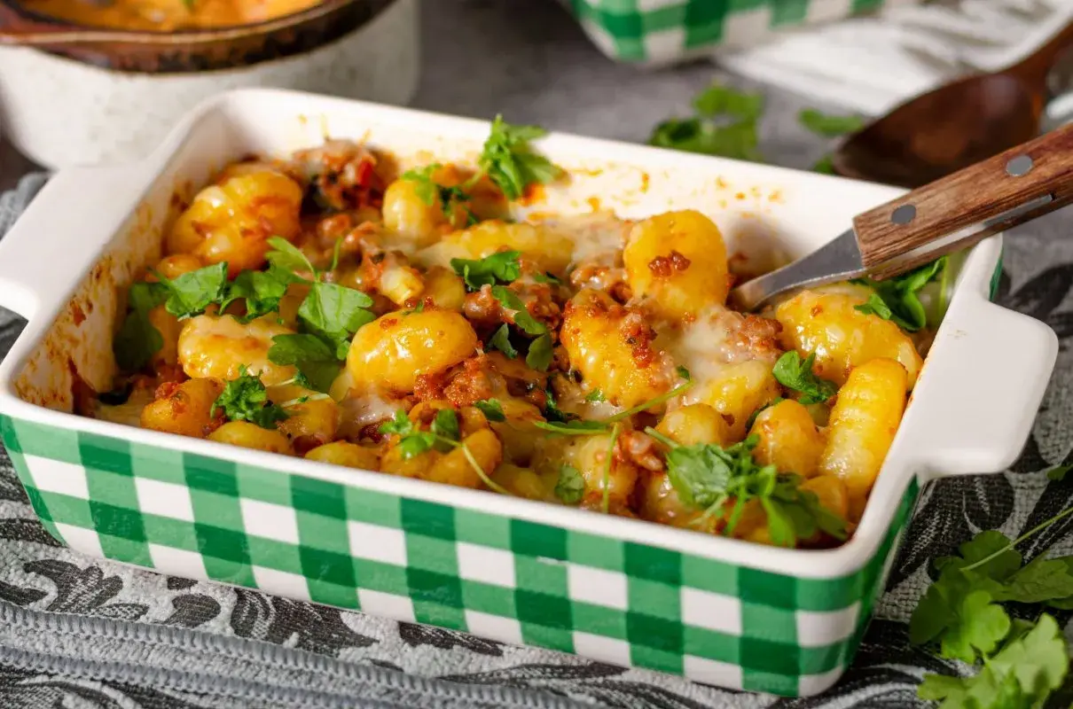 Zapiekane gnocchi z pomidorami i mozzarellą, posypane świeżą natką pietruszki, w zielono-białej kratce. Pyszne danie gotowe do podania.