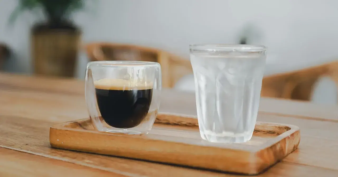 Szklanka espresso i szklanka wody z lodem na drewnianej tacy. Woda do espresso pomaga oczyścić kubki smakowe przed degustacją.