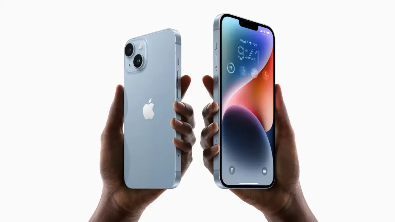 Dwie ręce trzymają jasnoniebieskie iPhone'y 14. Zastanawiasz się, czy oplaca sie kupic iPhone 14?