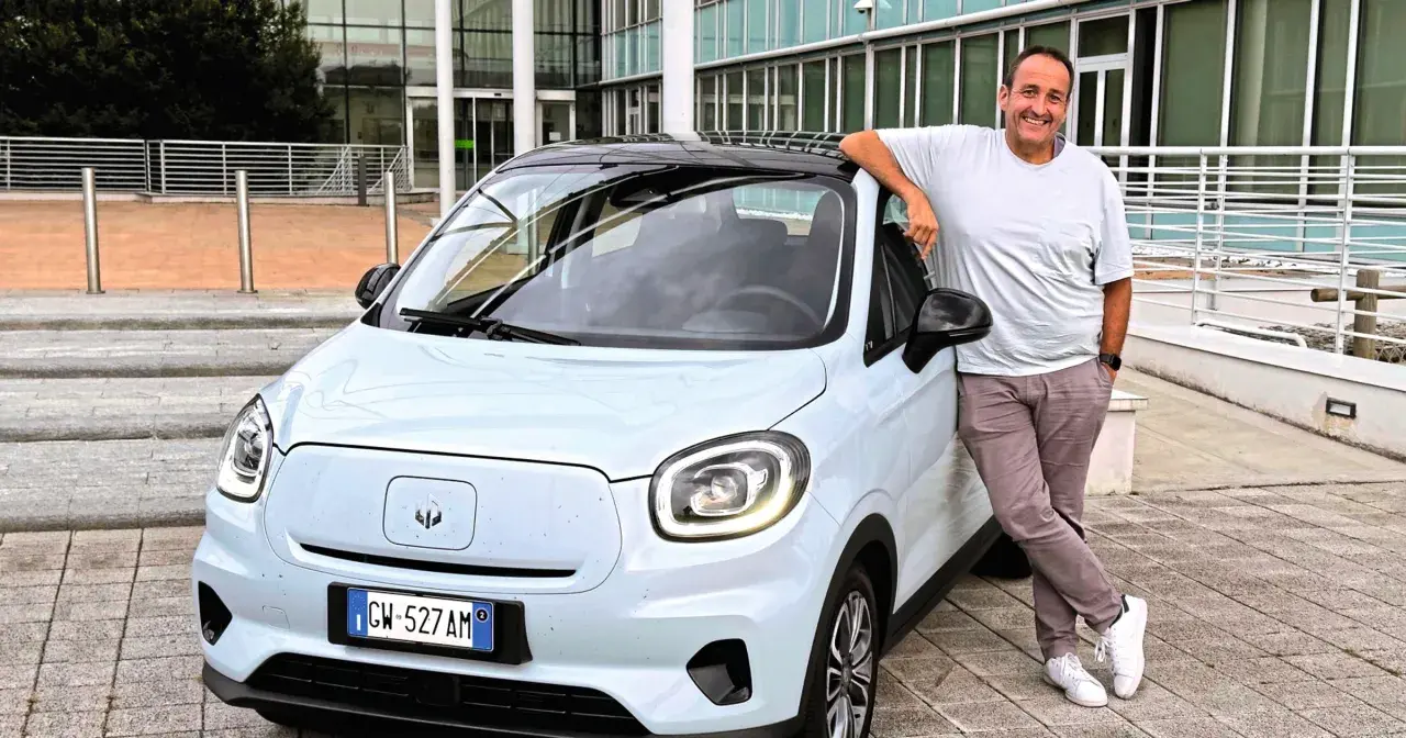 Uśmiechnięty mężczyzna opiera się o jasny samochód elektryczny Leapmotor T03.