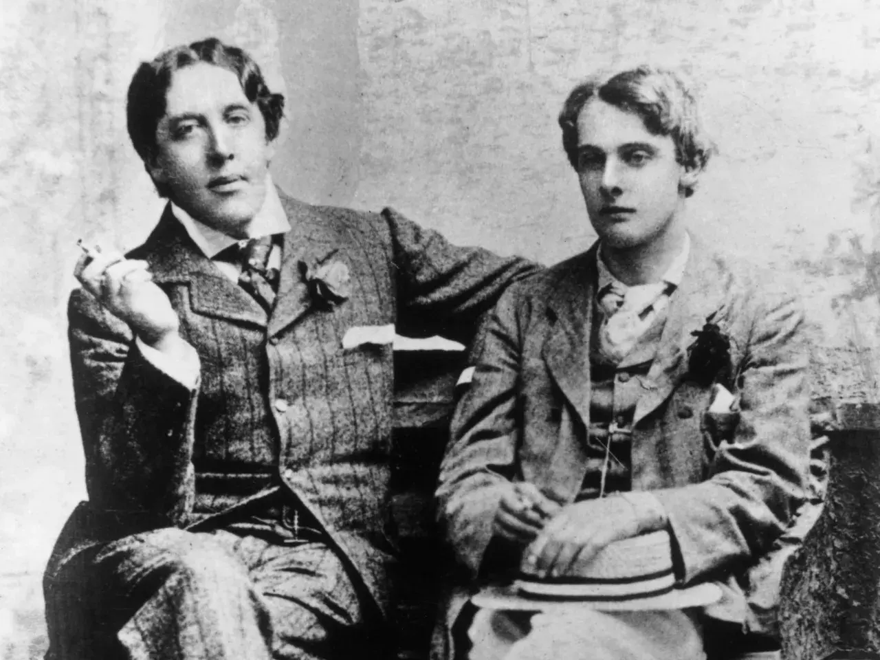 Oscar Wilde, lord elegancji i błyskotliwy pisarz, siedzi z młodym mężczyzną, trzymając papierosa.