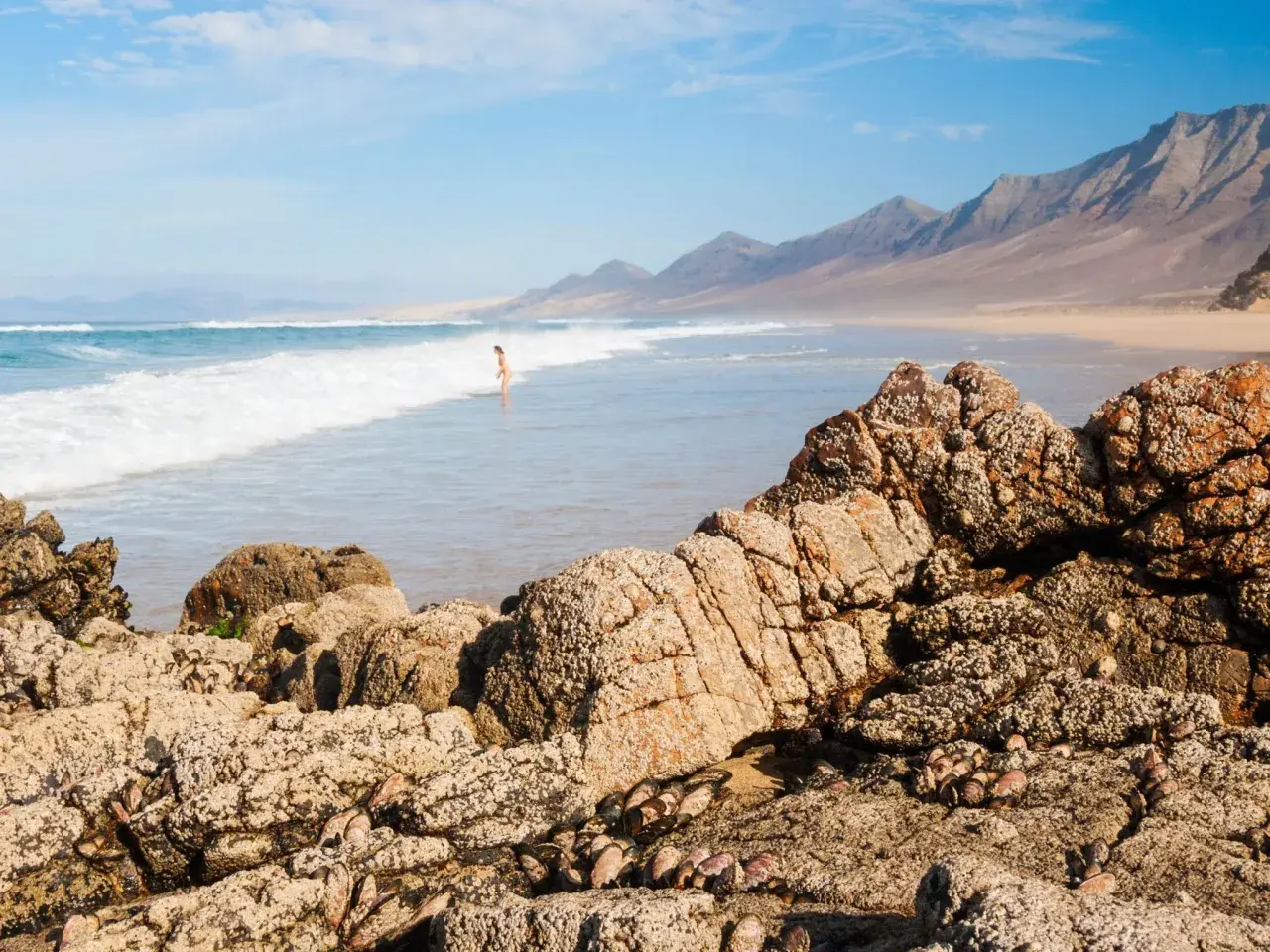 Una persona disfruta de las playas nudistas de Cantabria, con olas rompiendo en la costa y montañas al fondo.