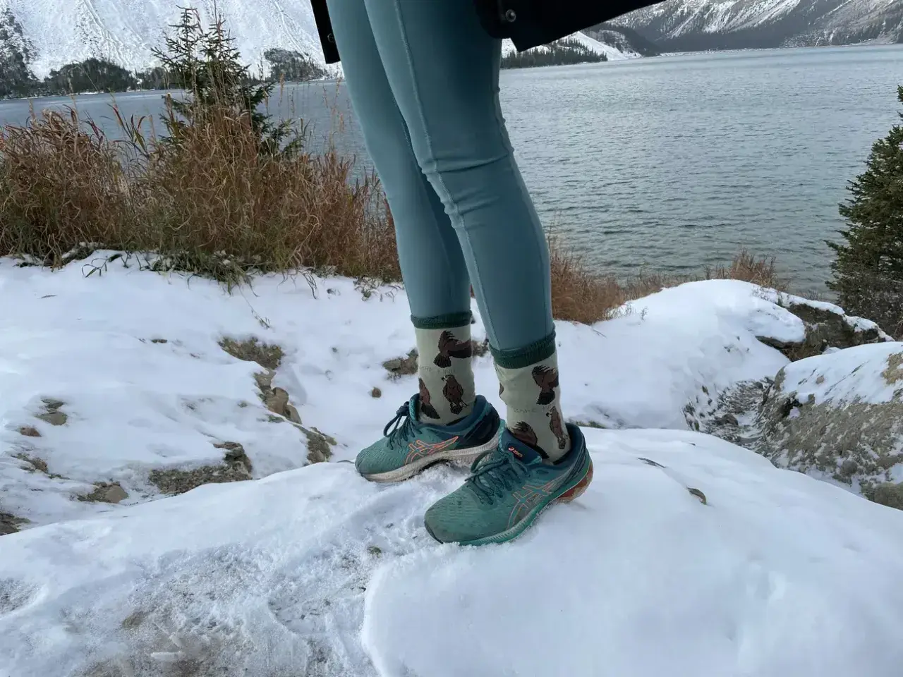 Wygodne leginsy w góry i buty do biegania na śniegu. W tle jezioro i ośnieżone szczyty.