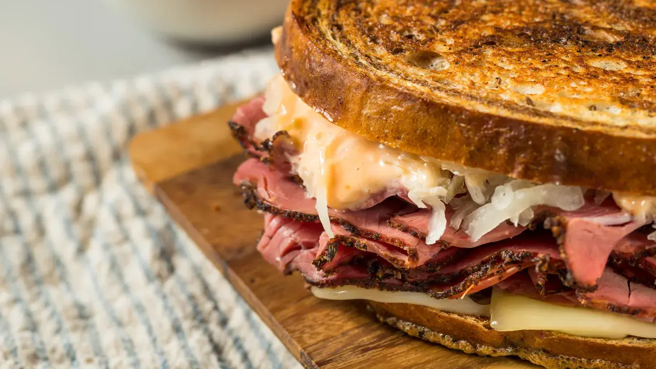 Un delicioso bocata de pastrami con pan tostado, queso fundido y chucrut.