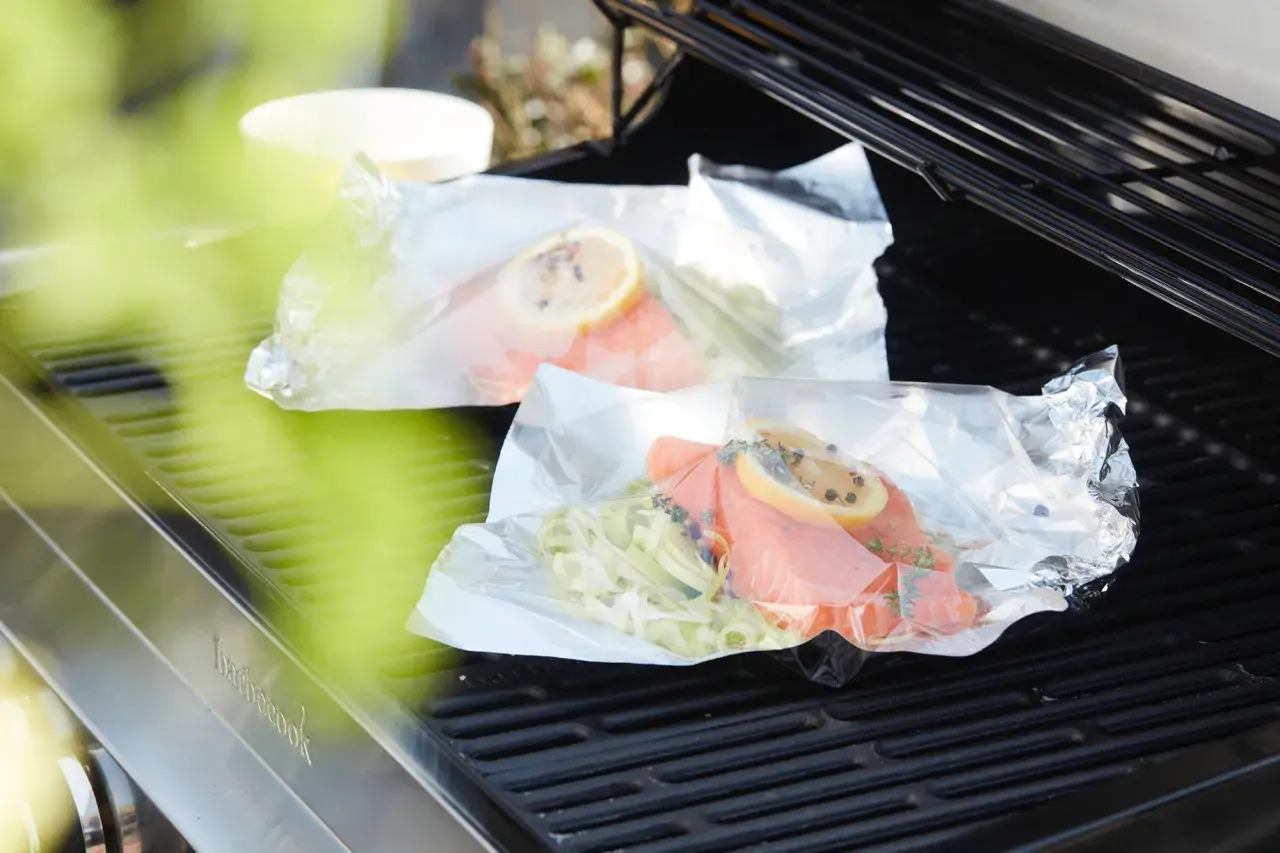 Deux papillotes de saumon en préparation sur un barbecue, prêtes à être cuites.