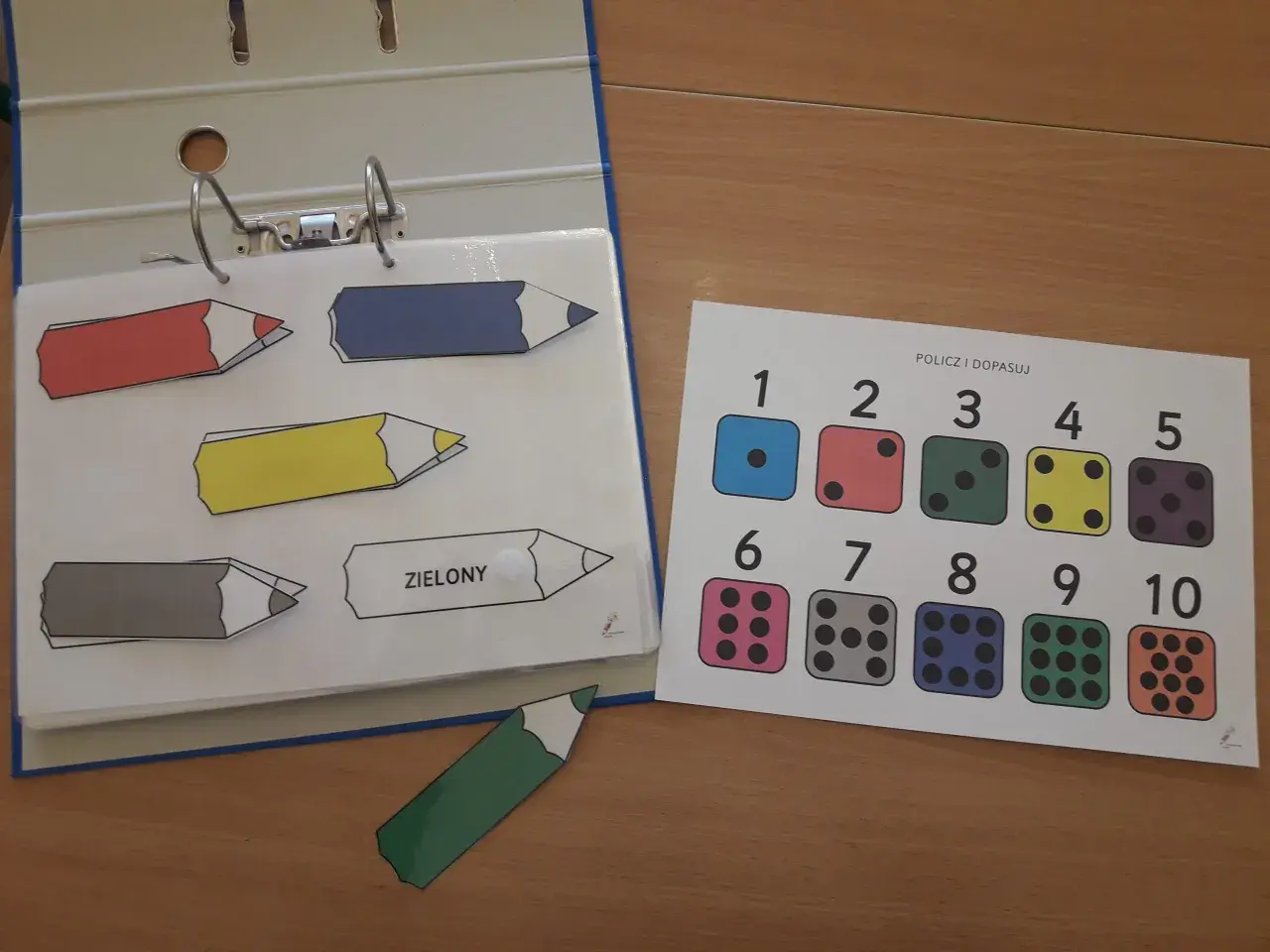 Kolorowe kredki i kostki do gry na karcie "Policz i dopasuj" to część edukacyjnych książeczek aktywizujących.