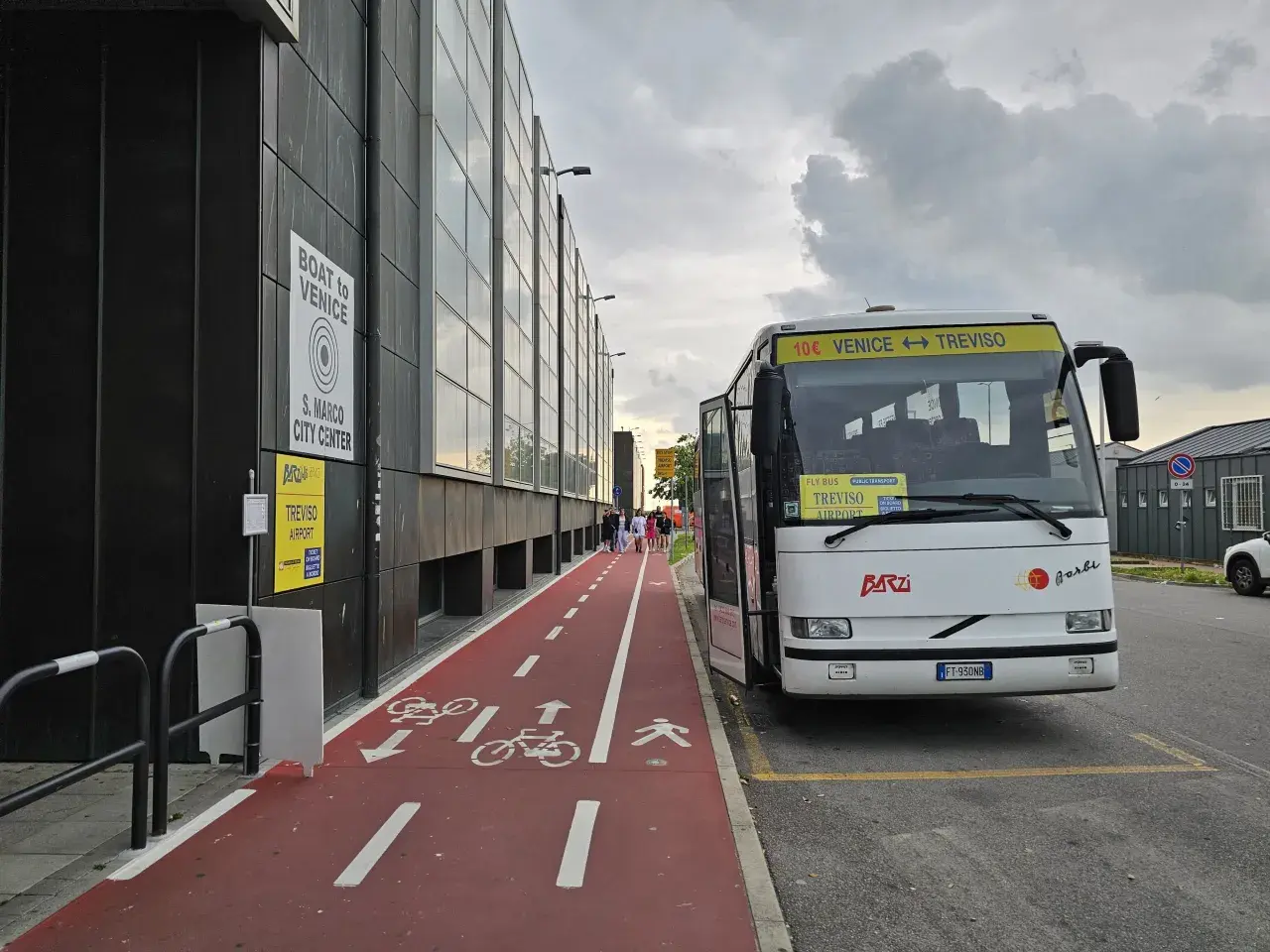 Autobus na lotnisku Treviso z napisem "Venice <-> Treviso". Czerwona ścieżka rowerowa i piesza obok budynku.
